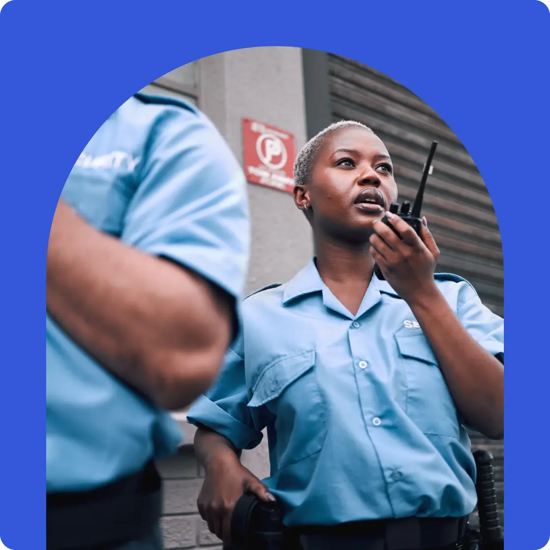 Security officer communicating via two-way radio during an active on-site operation outside a commercial building.