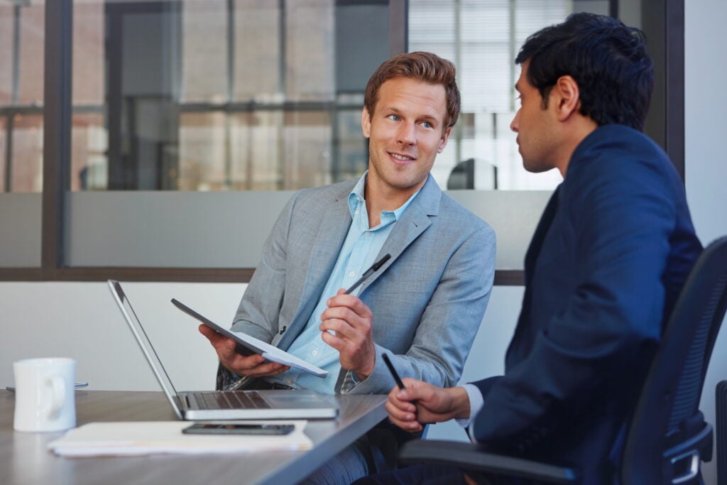 Two businessmen in a meeting, discussing documents at a conference table with a laptop open